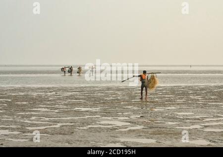 Pescatori che trasportano reti da pesca su pali oltre la spalla camminando sul mare a bassa marea; Chandipur, distretto di Baleswar, Stato di Odisha, India Foto Stock