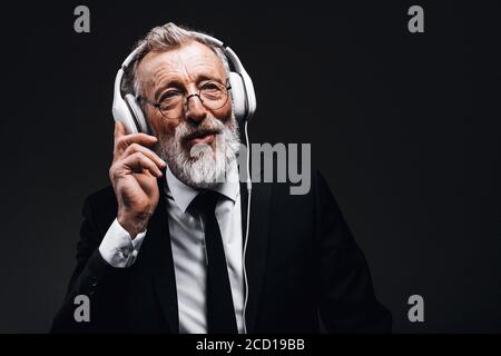 Studio isolato scatto di bell'uomo d'affari maturo dai capelli grigi con cuffie, ascoltando le canzoni ad alta voce, rilassandosi e riposandosi per la sua anima. Pisello Foto Stock