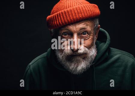 Nonno anziano dai capelli grigi che si sente sopravorato ed eccitato mentre racconta il suo viaggio in montagna. Uomo anziano vestito con cappello rosso lavorato a maglia e ho verde Foto Stock