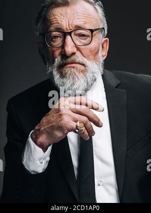 Uomo d'affari con cuscinetti maturi in occhiali e occhi sicuri esperti, vestito in abito nero formale pensando con la mano sotto il mento in posa isolato sopra Foto Stock