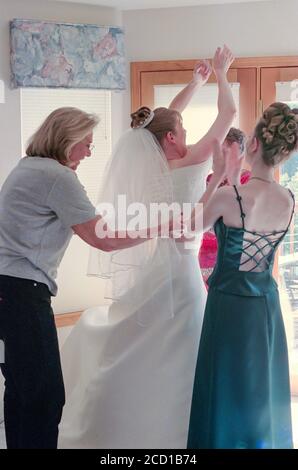 Madre e assistenti nuziali assistono la sposa giovane con il suo abito da sposa prima della cerimonia, Stati Uniti Foto Stock