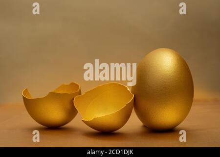 Uova d'oro e uova spezzate con tuorlo al sfondo dorato Foto Stock