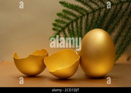 Uova d'oro e uova spezzate con tuorlo al sfondo dorato Foto Stock
