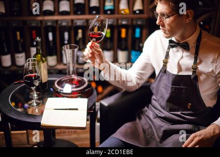 Cavist al negozio, sommelier al ristorante, critico. Degustazione di vini. Esperienza di degustazione in club, uomo che tiene un bicchiere di vino delizioso. Foto Stock