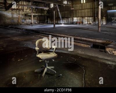 Vecchia sedia sporca seduta in acqua all'interno di una fabbrica industriale abbandonata Foto Stock