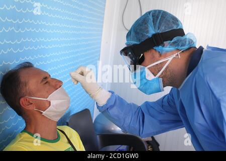 Un operatore medico che indossa indumenti protettivi raccoglie un bastoncino da Una persona durante un test Covid-19 al porto di Pireo Foto Stock