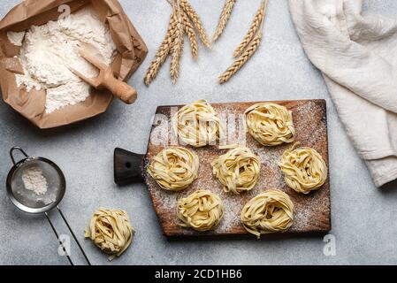 Tagliatelle. Pasta tradizionale italiana cruda fatta in casa su una tavola di legno su fondo grigio di cemento. Messa a fuoco selettiva Foto Stock