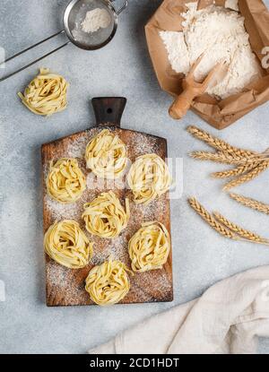 Tagliatelle. Pasta tradizionale italiana cruda fatta in casa su una tavola di legno su fondo grigio di cemento. Messa a fuoco selettiva Foto Stock
