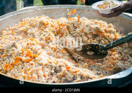 Cucina Uzbeko pilaf. Cibo nazionale. Arrostire la carne in un grande calderone. Pentola grande con pilaf uzbeko Foto Stock