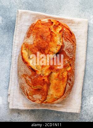 Pane di grano tradizionale appena sfornato fatto in casa da vicino su un tovagliolo di lino su uno sfondo grigio di cemento. Il concetto di cottura. Messa a fuoco selettiva Foto Stock