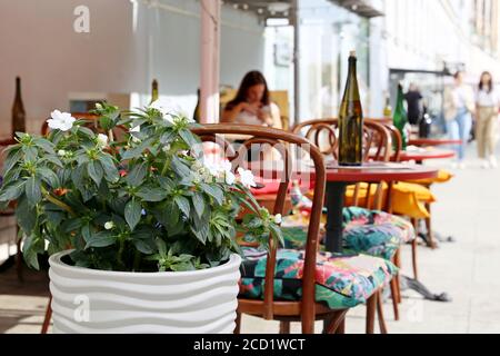 Street cafe in una città, tavoli con bottiglie in un ristorante all'aperto, ambiente elegante per celebrazione e data. Pentola con fiori e sedie vintage Foto Stock