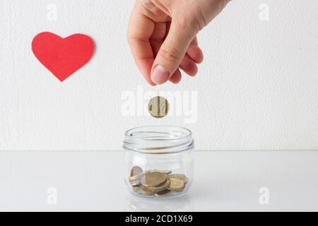 Mano che mette la moneta in un vaso su sfondo bianco. Risparmio di denaro, medicina o concetto di donazione. Foto Stock