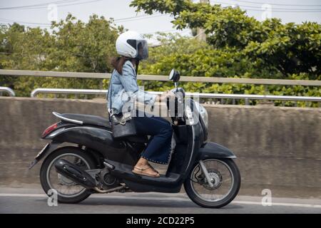 Una giovane donna che guida una moto su strada. Ragazza asiatica ride scooter in strada. Foto Stock