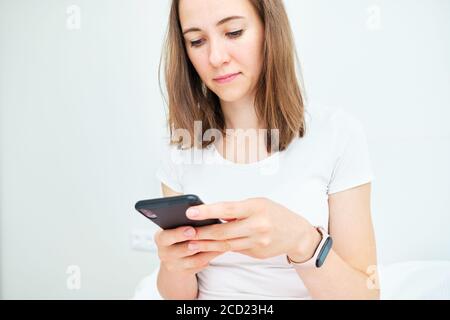 Giovane donna caucasica usa il telefono a casa. Foto Stock