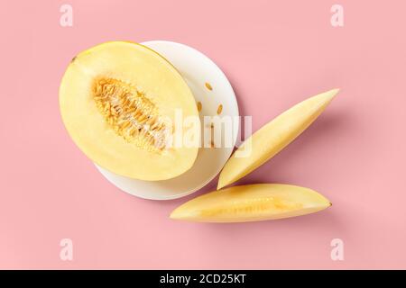 Metà di melone giallo maturo sulla piastra bianca e due fette su sfondo rosa pastello. Vegetariano, dieta di cibo crudo e concetto di alimentazione sana. Foto Stock