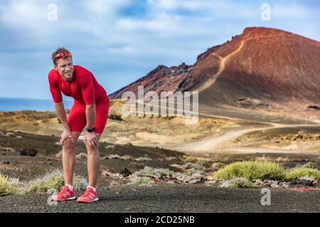 Corridore stanco sulla pista si sente esausto e disidratato dal calore. Atleta con smartwatch che prende una pausa catturando il respiro guardando Foto Stock