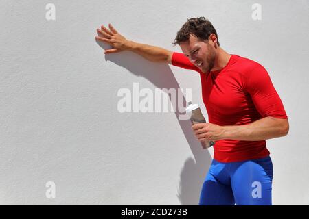 Dopo l'allenamento, stanco, esausto e disidratato man Runner che beve una bottiglia d'acqua. Running persona che prende una pausa dopo corsa. Atleta di fitness che respira dal sole Foto Stock