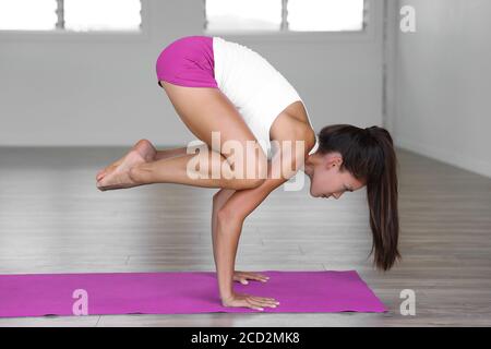 Yoga studio donna fare corvo posa in palestra classe. L'equilibrio delle braccia di addestramento della ragazza sul tappeto di esercitazione. Foto Stock