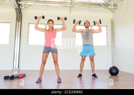 Coppia di idoneità che lavora insieme le braccia di addestramento che fanno la spalla in alto premere con pesi dumbbells o in piedi esercizio stampa dumbbell a. palestra Foto Stock