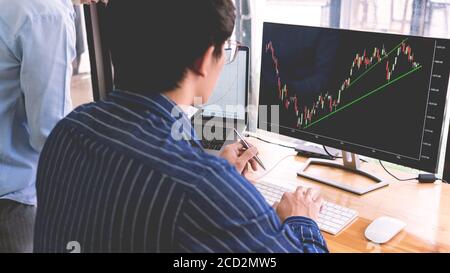 broker mostrando un po 'ascendente al suo collega di pianificazione e analisi grafico delle negoziazioni di borsa con i dati di grafico di borsa su più schermi del computer Foto Stock