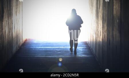 Una figura isolata e solitaria svanisce dirigendosi o camminando verso una luce luminosa alla fine del tunnel. Dolore, morte, suicidio morente, concetto di fede. Crossin Foto Stock