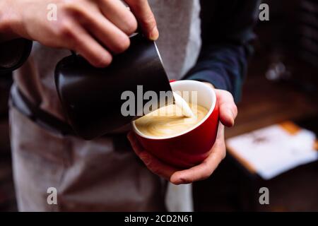 Il barista versa il latte fresco in una tazza di caffè. latte art Foto Stock