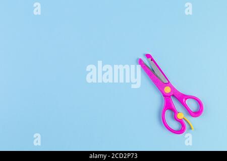 Foto minimalista delle forbici rosa per bambini su sfondo blu. Concetto di ritorno a scuola con cancelleria. Con spazio di copia, modello per testo o disegno. Foto Stock