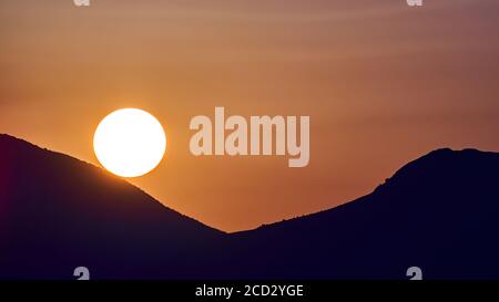Mercato dell'energia solare: Il disco solare luminoso al tramonto sembra rotolare sopra le montagne come su un grafico. Simbolico di Market Outlook Foto Stock