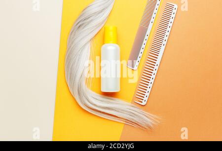 Bottiglia di shampoo arancione con ciocca di capelli biondi e pettini. Attrezzature per parrucchieri, attrezzature per parrucchieri in salone di bellezza, barbiere Foto Stock