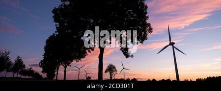 turbine eoliche e alberi formano silhouette contro il tramonto colorato Foto Stock