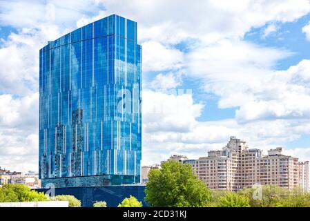 La splendida facciata in vetro dell'edificio moderno riflette il cielo blu e le nuvole bianche nelle sue finestre sullo sfondo del paesaggio cittadino. Foto Stock