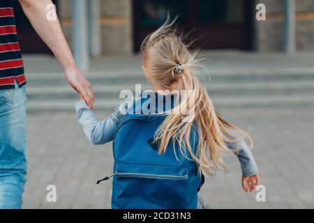 Vista posteriore del padre che torna a scuola con la sua zaino da trasporto per figlia Foto Stock