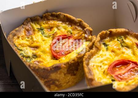 Due piccole tartine di pomodoro in primo piano nella scatola da asporto - sfondo saporito mini quiche con messa a fuoco selettiva Foto Stock