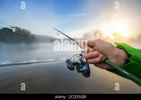 Primo piano di pescatore che tiene canna da pesca. Bella luce tramonto su sfondo Foto Stock