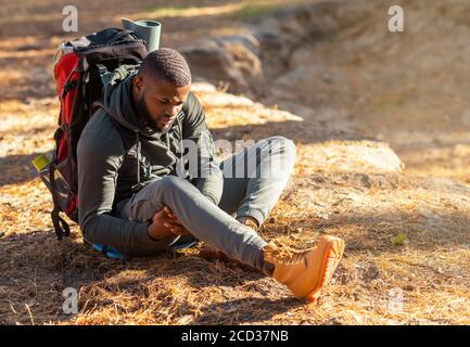 Ragazzo nero seduto a terra, strofinando il ginocchio Foto Stock