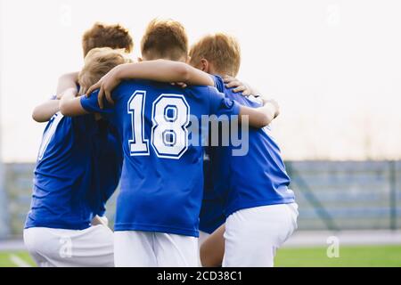 I bambini giocano gli sport in una squadra. Ragazzi Huddling prima del gioco. Kids Sports Team United Ready to Play Match. Ragazzi di età scolastica in uniformi di sport blu Foto Stock