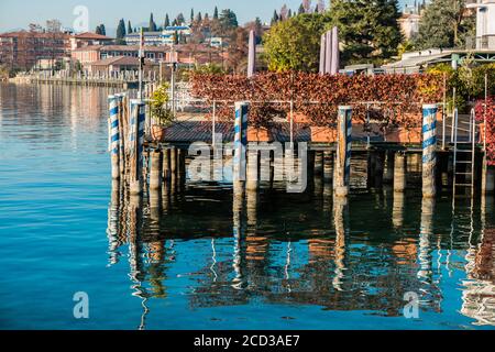 Un antico molo in legno testurizzato e colorato sul Lago di Garda Sirmione. Nell'acqua liscia si riflette il piccolo molo per le imbarcazioni da diporto. Foto Stock