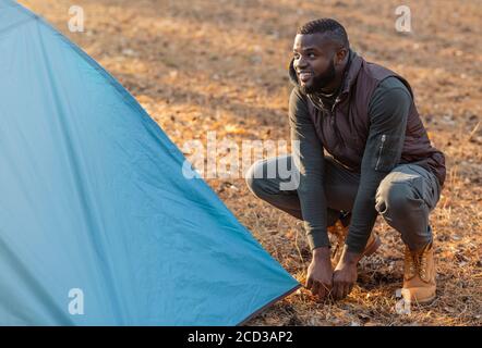 Ragazzo nero che istituisce la tenda blu nella foresta Foto Stock