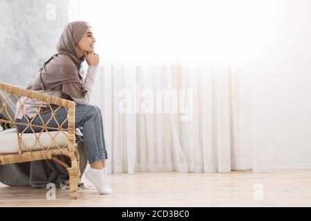 Ragazza musulmana pensiva in Hijab che si rilassa nella sedia di Wicker a. Casa Foto Stock