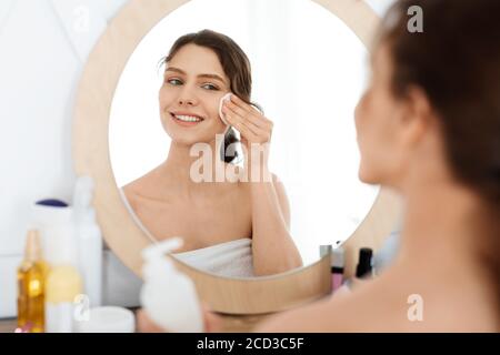 Ragazza allegra che pulisce il suo viso, utilizzando tamponi di cotone Foto Stock