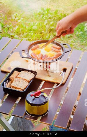 Camping alimentare fare. Uova fritte e salsicce in padella sul bruciatore turistico a gas. Camper preparare cibo nella foresta. Foto Stock