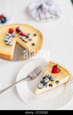 Pezzo di cheesecake fatto in casa con fragola fresca e mora su un piatto bianco su un tavolo. Foto Stock