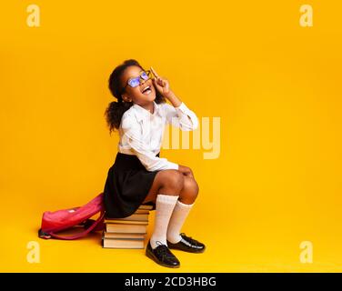 Schoolgirl avendo idea che punta il dito in su seduto sui libri, studio Foto Stock