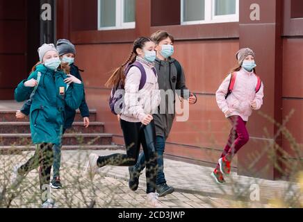 Bambini studenti in maschere mediche lasciare la scuola. Foto Stock