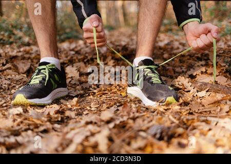 Il concetto di sport. Un uomo lega le sue scarpe alle sue sneakers. Vista ravvicinata delle gambe e delle braccia Foto Stock