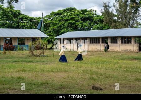 Isola di Pemba, Zanzibar, Tanzania - Gennaio 2020: Due ragazze della scuola primaria tengono il loro libro sulla testa e si muovono attraverso la scuola Yard in uniforme Foto Stock