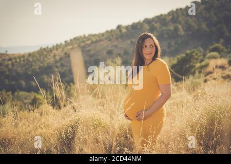 Donna felice incinta che tocca il ventre. Intera lunghezza incinta bellezza giovane madre ritratto all'aperto, carezzandogli il ventre e sorridendo. Gravidanza sana Foto Stock