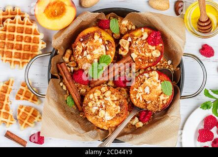 Pesche al forno con ricotta, mandorle, biscotti sbriciolati o cialde viennesi (belghe) e cannella, servite con miele, lamponi e menta. Gou delizioso Foto Stock