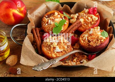 Pesche al forno con ricotta, mandorle, biscotti sbriciolati e cannella, servite con miele, lamponi e menta. Delizioso dessert gourmet. Messa a fuoco selettiva Foto Stock