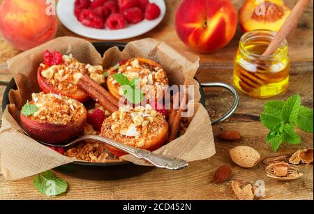 Pesche al forno con ricotta, mandorle, biscotti sbriciolati e cannella, servite con miele, lamponi e menta. Delizioso dessert gourmet. Messa a fuoco selettiva Foto Stock